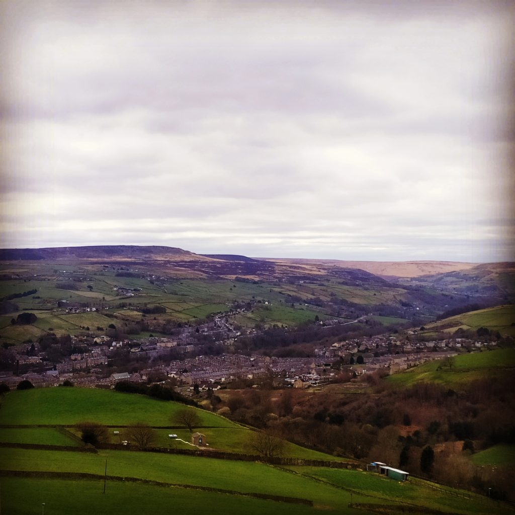 Looking up the Colne Valley from Slaithwaite towards Marsden from the side of Pole Hill to the north. Villages in the valley bottom, farms dotted along the valley sides and moorland tops to the hills. Marsden Moor and Saddleworth in the distance